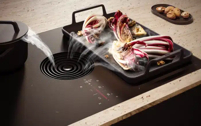 Induction cooktop with a grill tray of roasted red and white onions steaming, walnuts on a tray in the background.