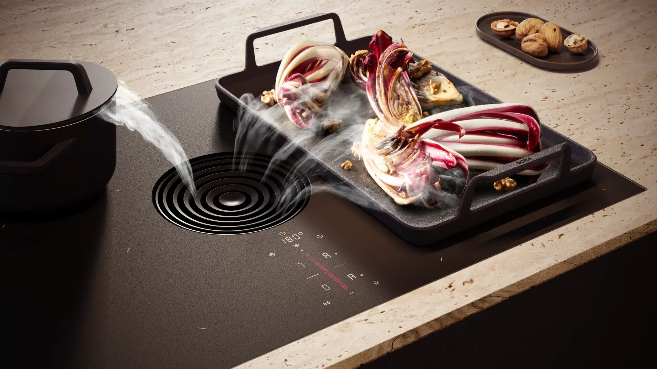 Induction cooktop with a grill tray of roasted red and white onions steaming, walnuts on a tray in the background.
